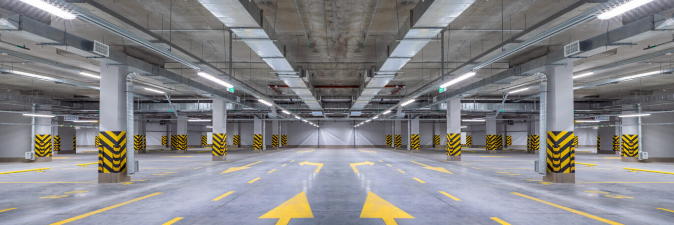 Een parkeergarage met een mooie industriële vloer. De vloercoating is afgewerkt in het grijs met bijbehorende gele pijlen en afbakeningen